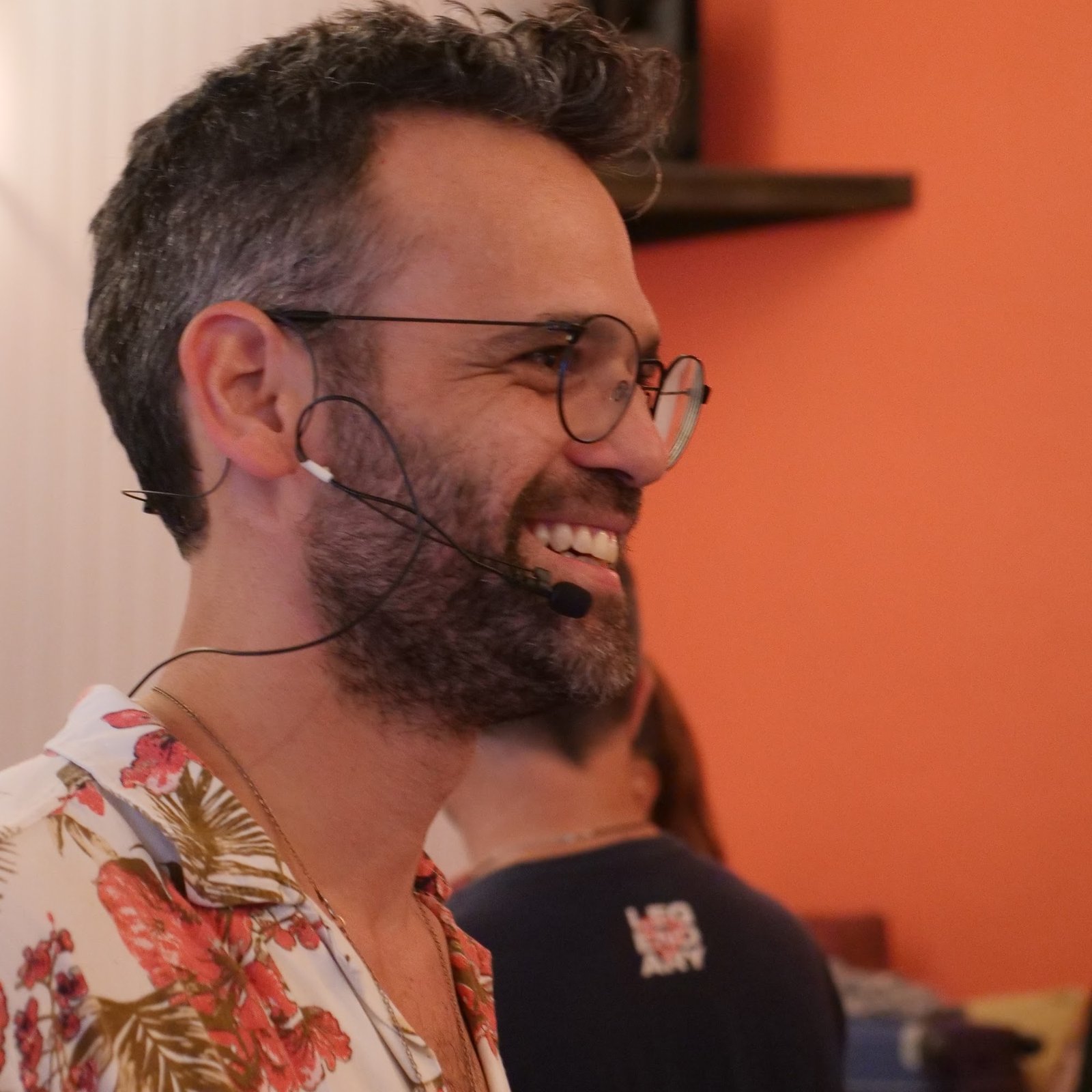 סשה בלבין צוחק באמצע הנחיית סדנה, מיקרופון מדונה על האוזן
